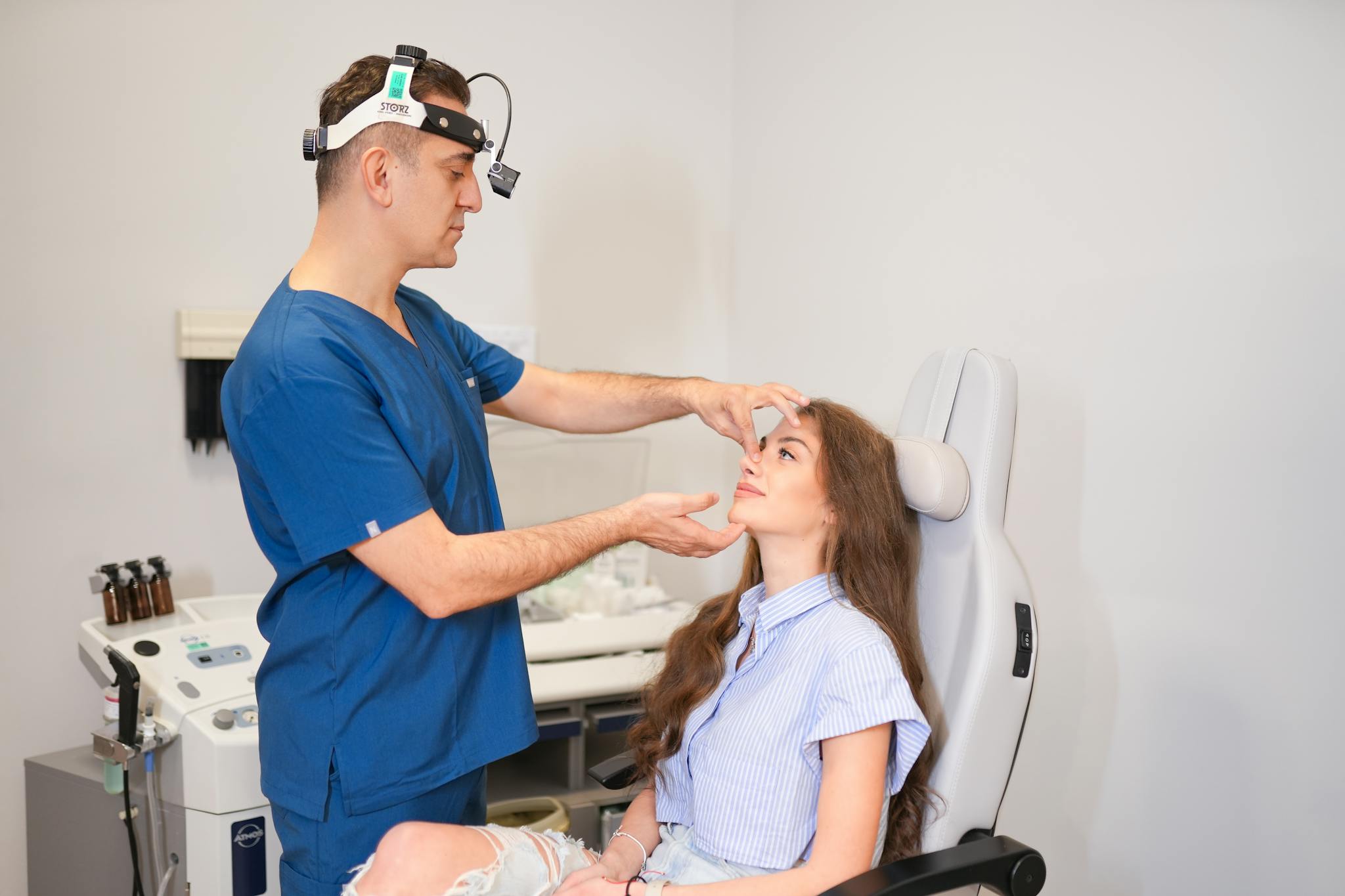 A plastic surgeon examines a patient's nose in a modern clinic setting in Istanbul.