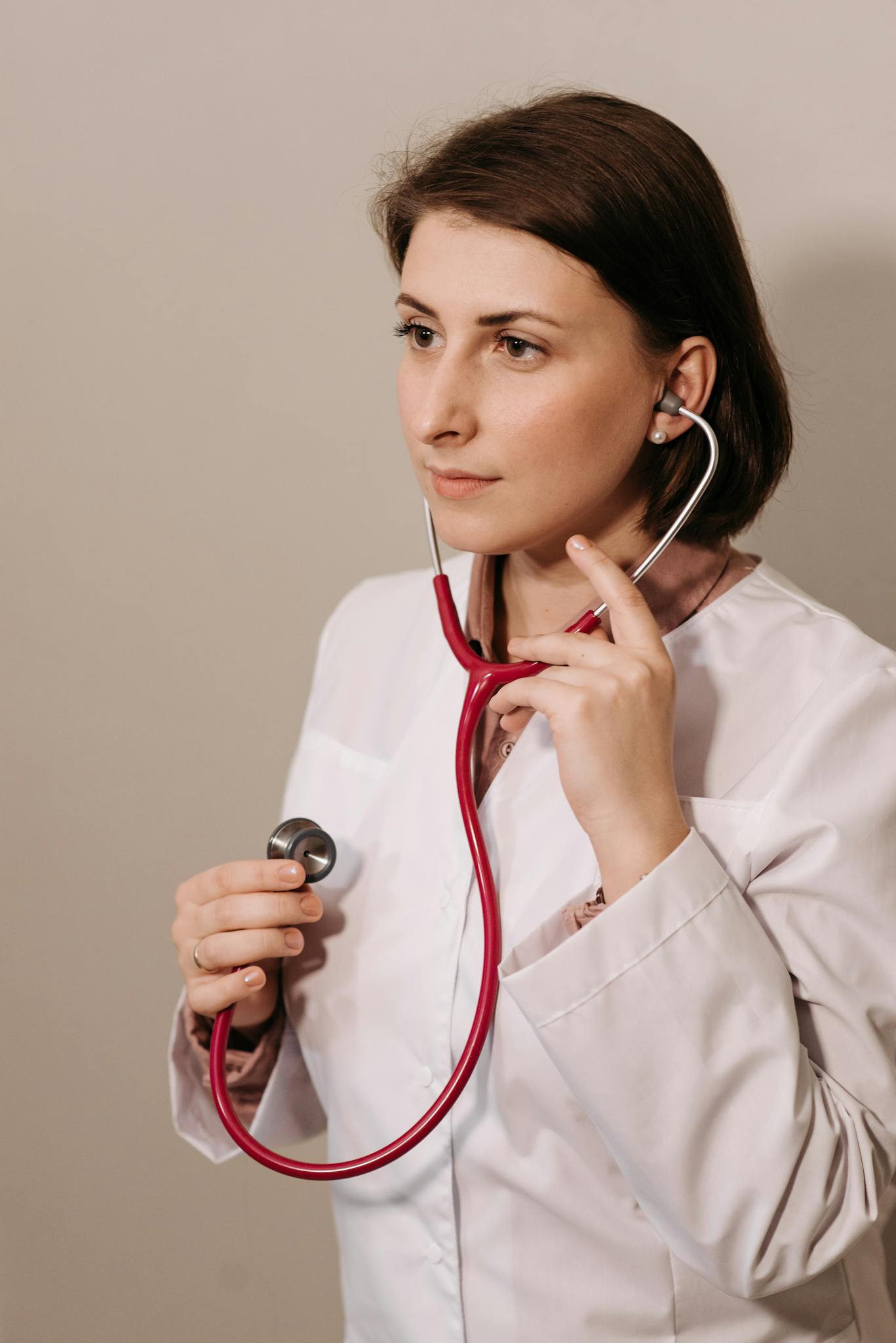 Confident female doctor in lab coat using stethoscope during medical examination.