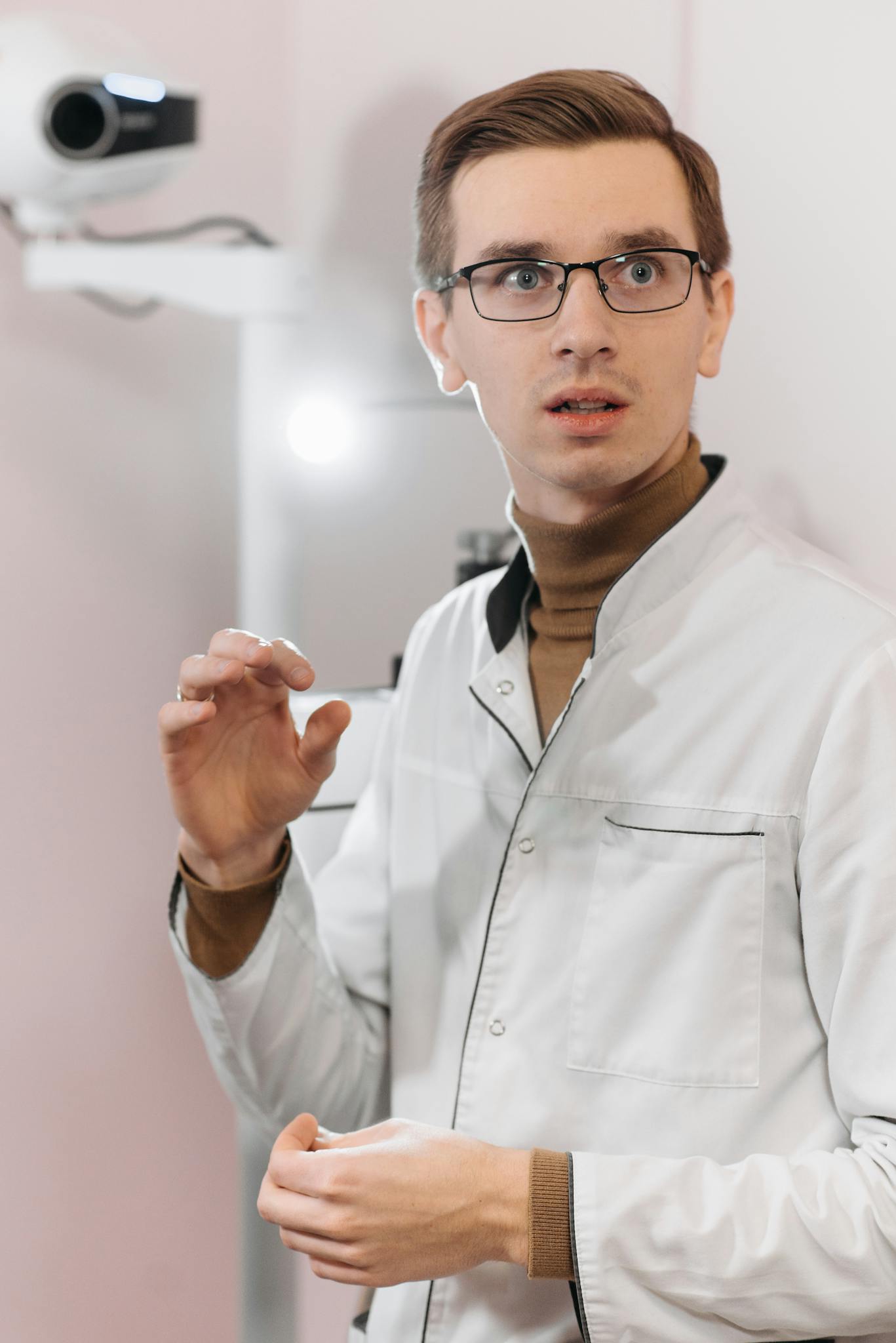 Young male doctor in eyeglasses and medical gown looking attentive.